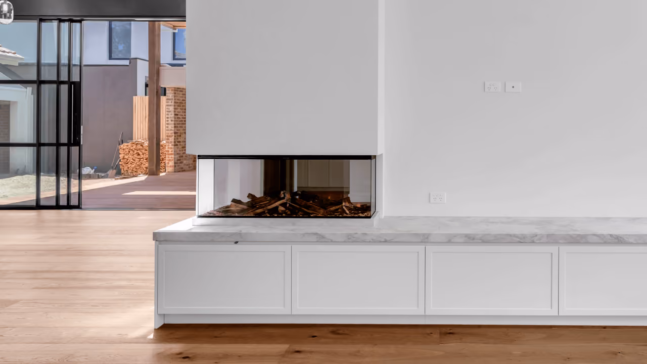 Modern room with a glass three-sided fireplace and white cabinetry under a marble countertop.
