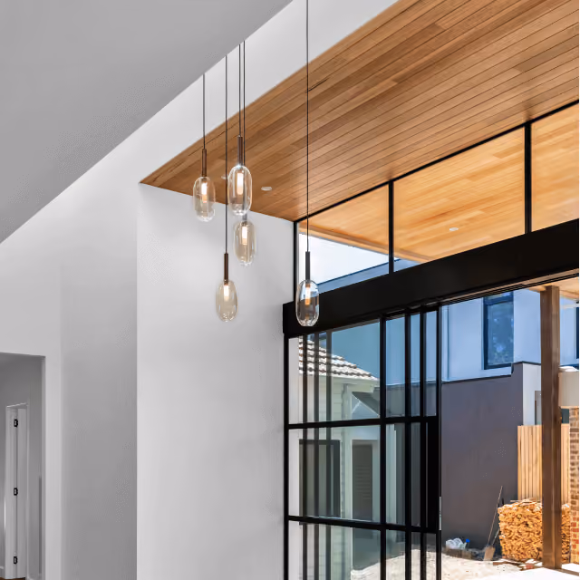 Modern interior with hanging glass pendant lights and large black-framed windows under wood ceiling.