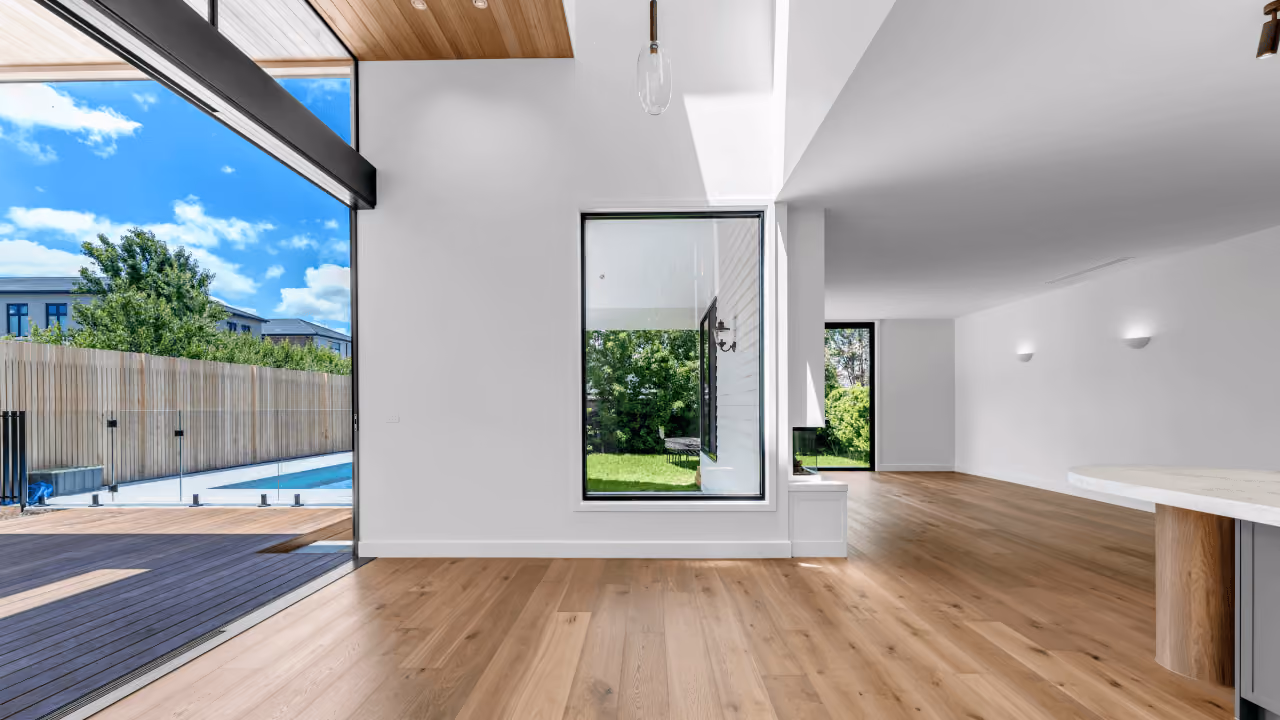 Modern empty room with wood floors, white walls, large window, and sliding glass door to backyard.