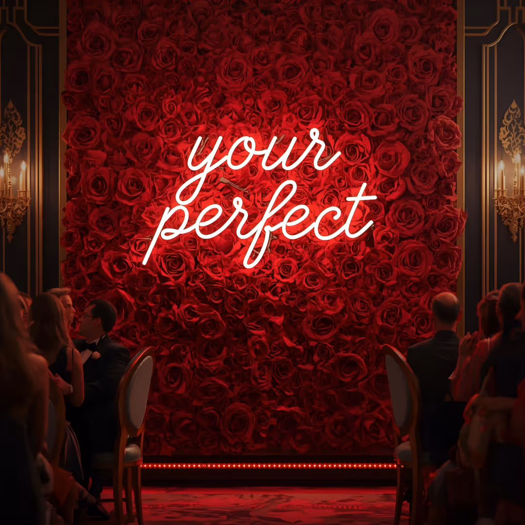 Red rose wall with illuminated white script reading 'your perfect' at a formal event.