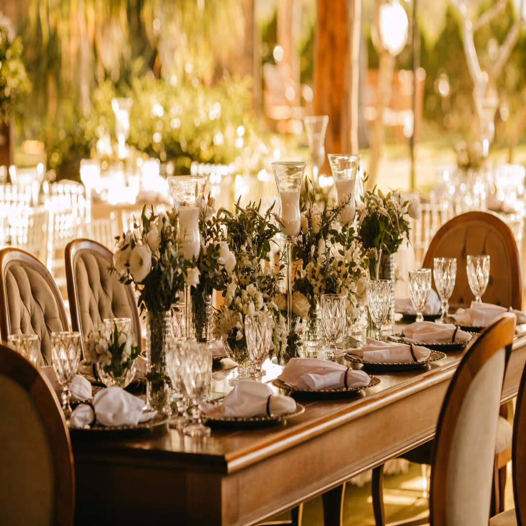 Elegant dining table set with white napkins, crystal glasses, and flower centerpieces in warm light.