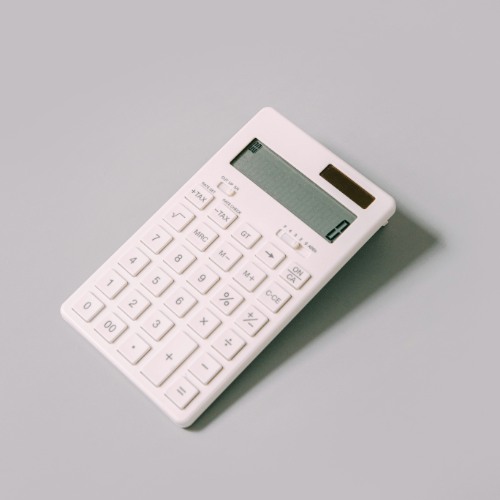 A minimal white calculator resting on a light grey surface, displaying the number zero on its screen.