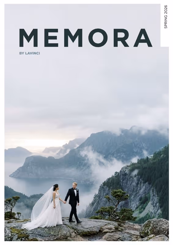 Bride and groom holding hands on rocky cliff overlooking misty mountains and lake.