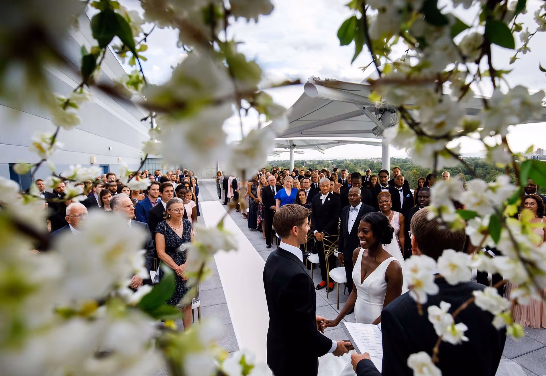 Bride and groom holding hands at outdoor wedding ceremony with guests seated facing them.