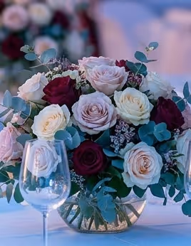 Bouquet of mixed red, white, and pale pink roses in a round glass vase with green foliage.