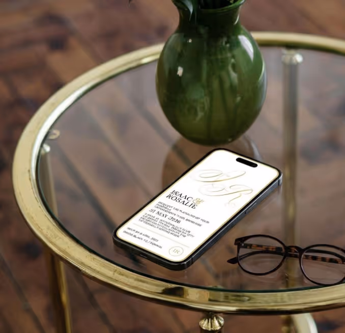 Black smartphone on a glass table next to tortoiseshell eyeglasses and a green vase with a plant.