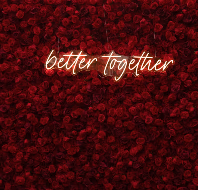 Neon sign reading 'better together' over a dense wall of red roses.