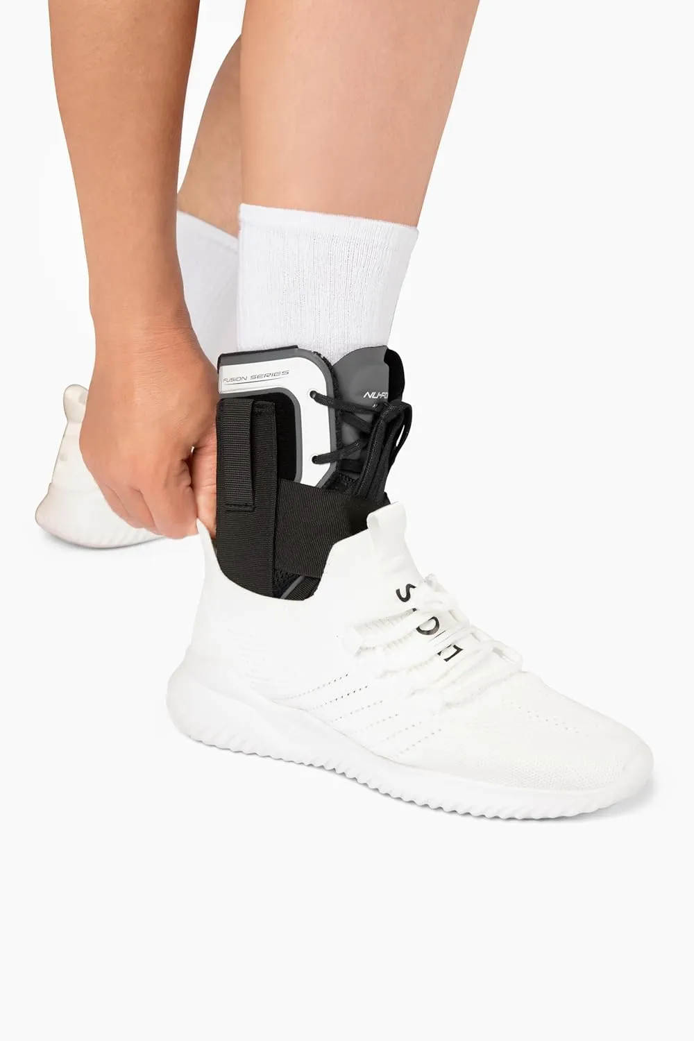 Person wearing white sneaker and white sock, adjusting a black and white ankle brace labeled Fusion Series.