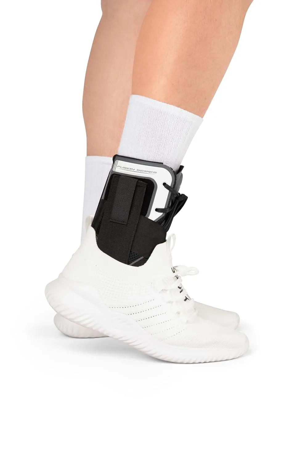 Person wearing white sports shoes and ankle brace with black and white straps on a white background.