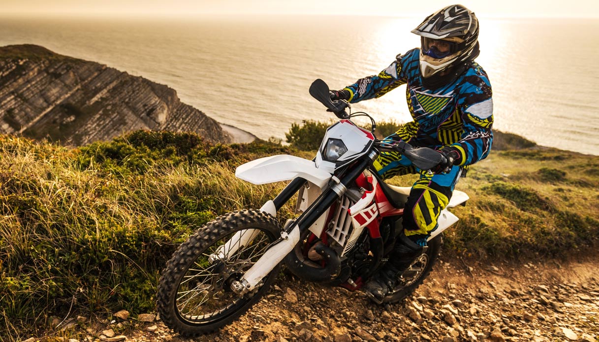An enduro bike racing through rough terrain, with an ocean on the background.