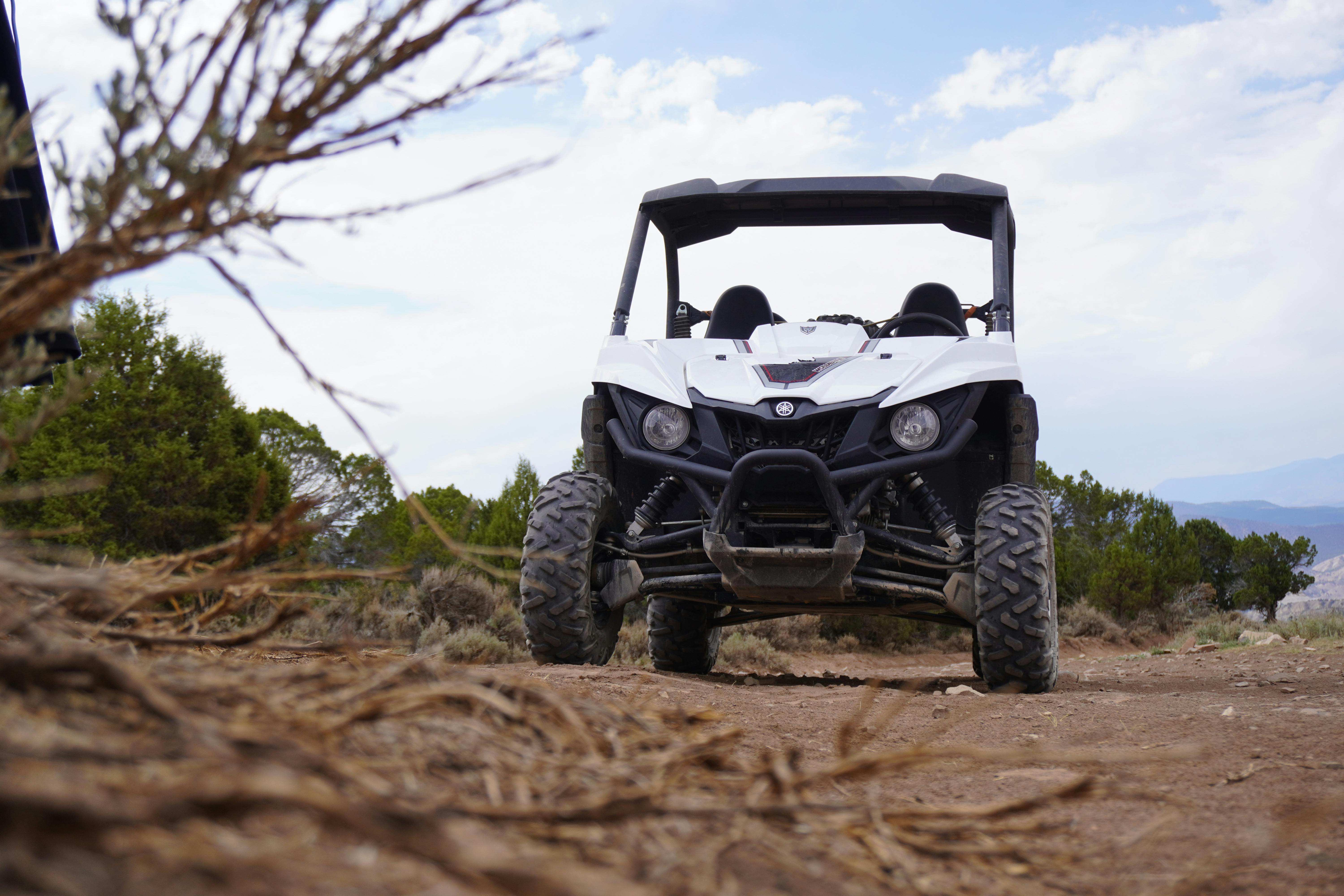 An UTV parkedin on top of a hill or mountain, in dirt, surrounded by trees and bushes.