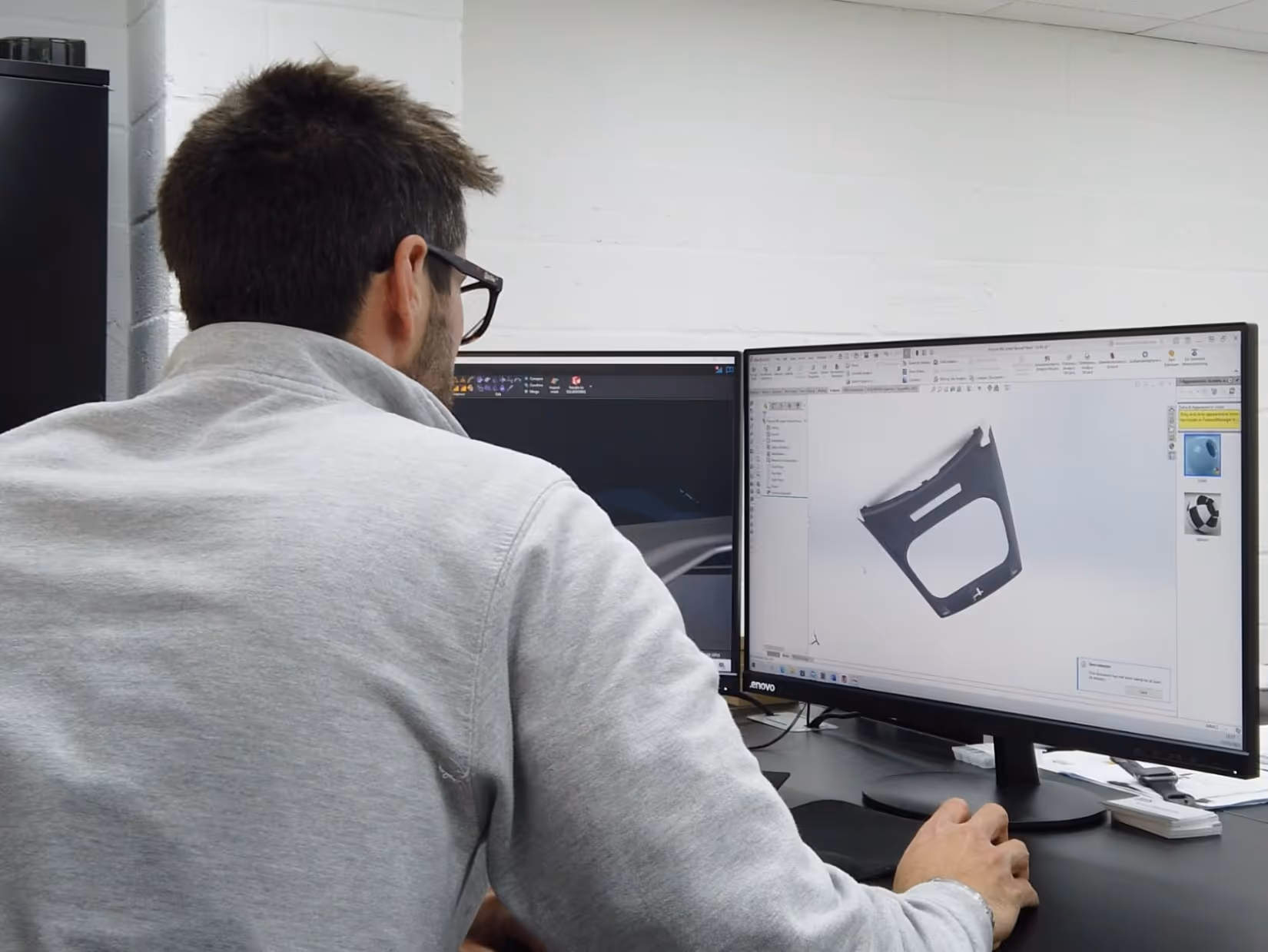 Man working on 3D modeling software displayed on dual computer monitors.