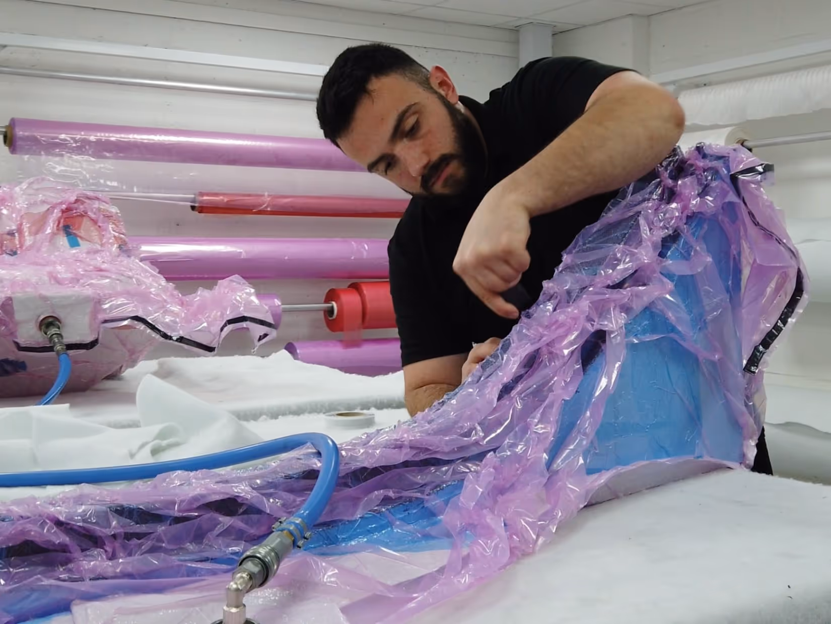Man inspecting or assembling a large translucent plastic piece with blue and purple hues in a workshop setting.