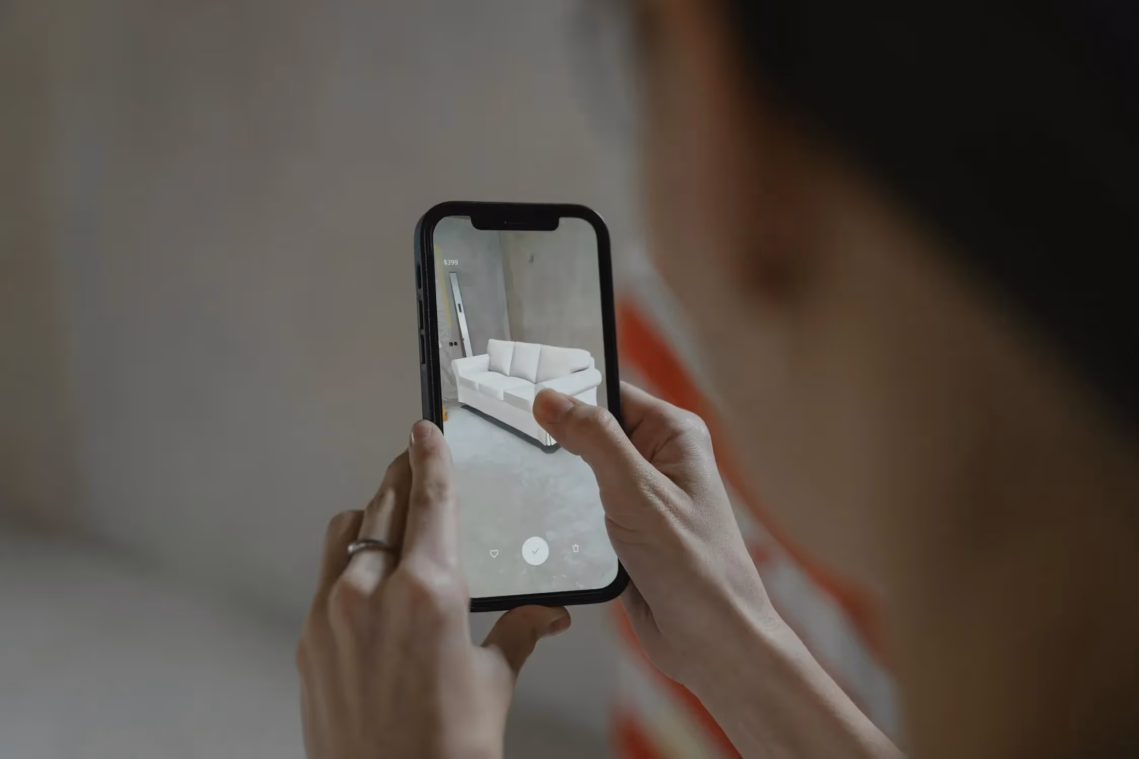 A person using a smartphone's augmented reality (AR) to visualize a white sofa in their living space, enhancing the online shopping experience.