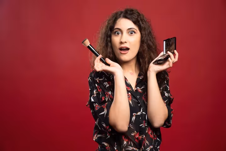 A surprised woman holding a makeup brush and compact, showcasing beauty product engagement