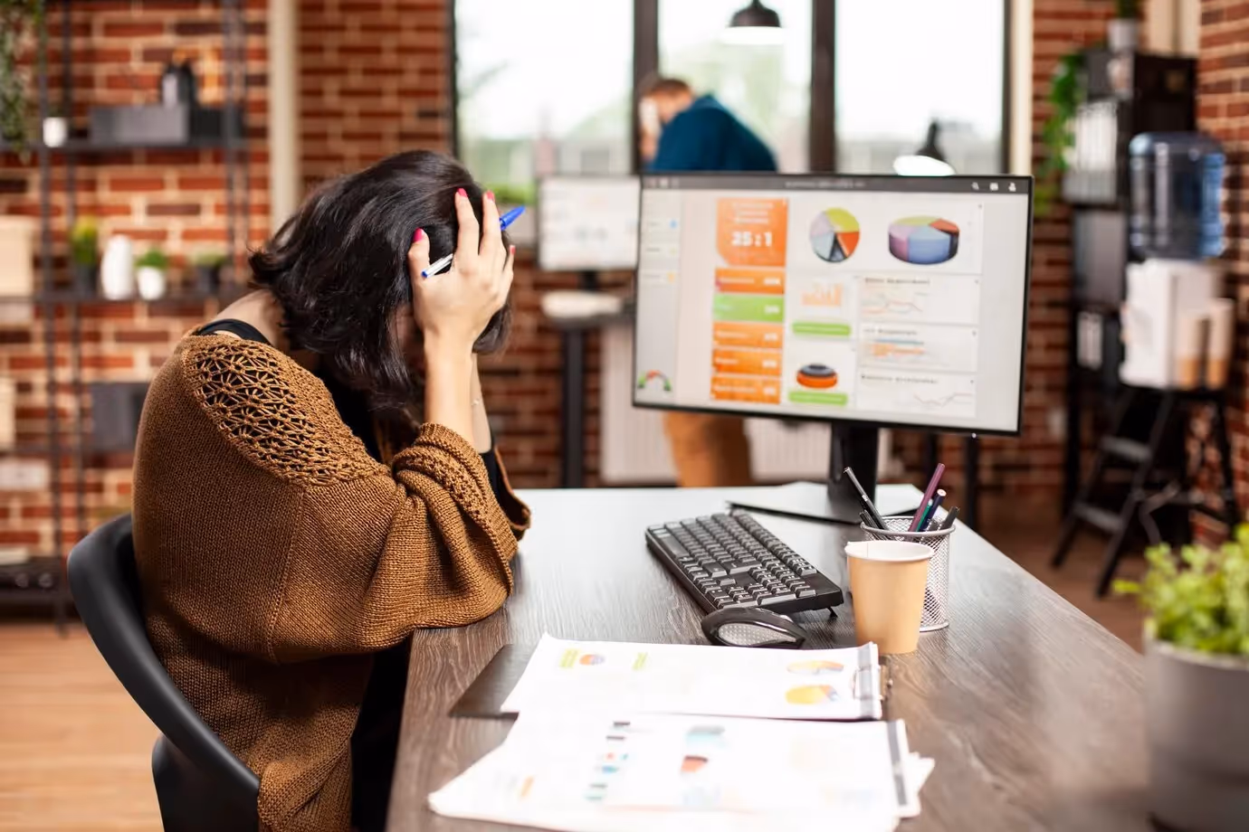 Stressed woman at desk holding her head in frustration while viewing marketing analytics on screen, illustrating challenges in managing ineffective personalization strategies.
