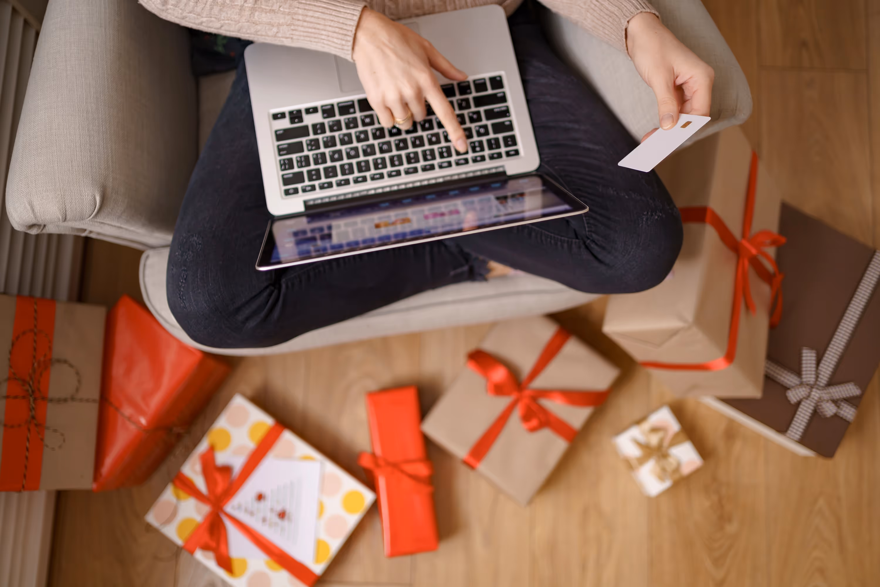 Person shopping online using a laptop and holding a credit card, surrounded by gift-wrapped packages through 