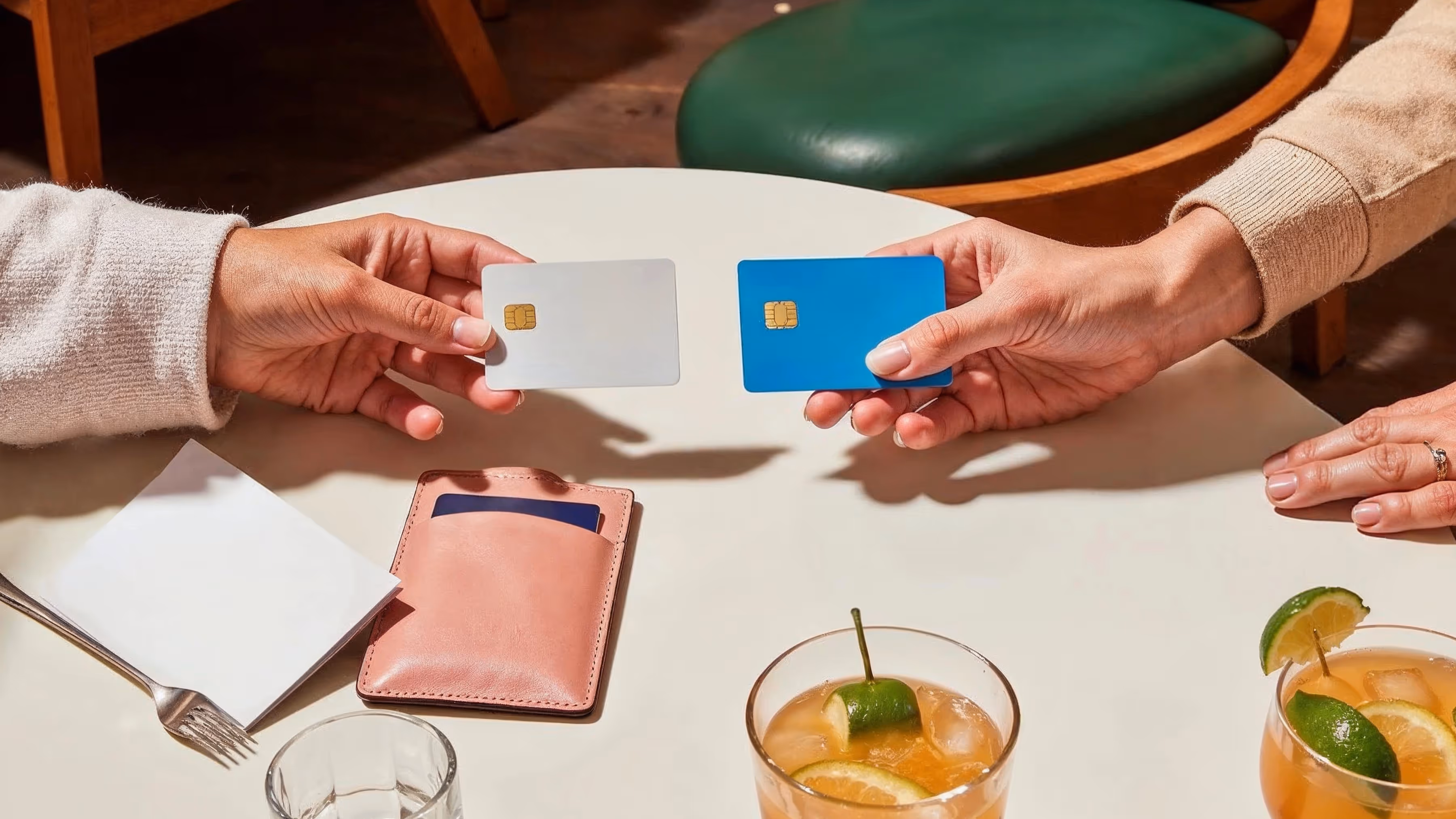 Two people exchanging blank credit cards at a cafe table, symbolizing points-based loyalty rewards through purchases.