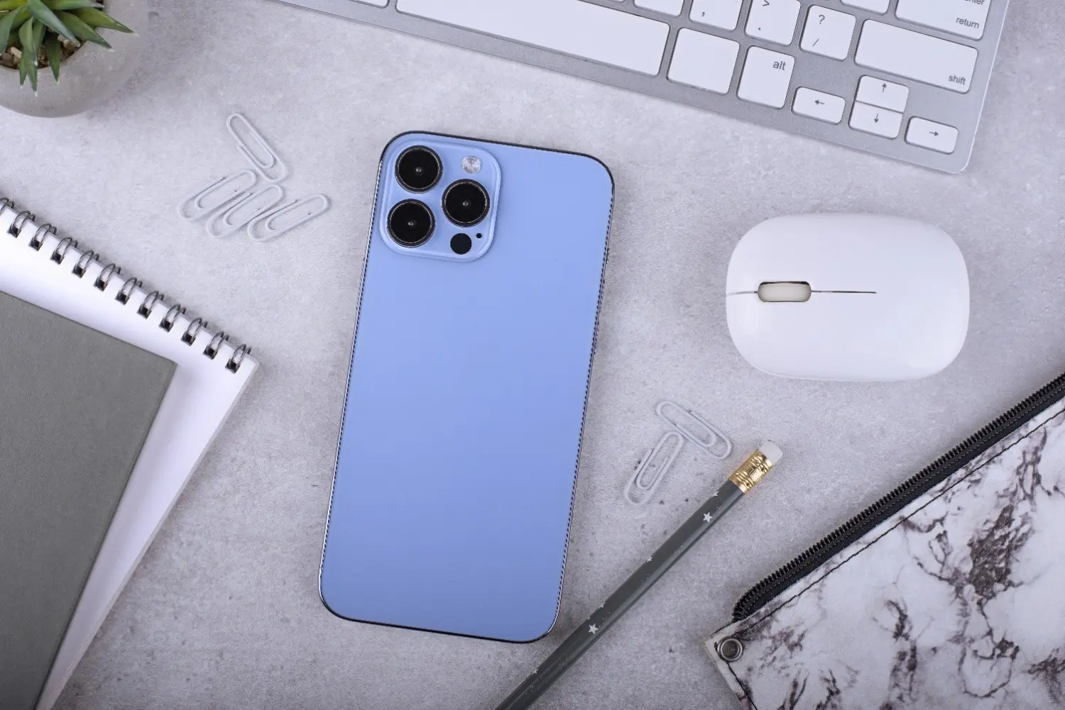 Blue Apple iPhone on a desk with keyboard, mouse, notebook, pencil, and office accessories.