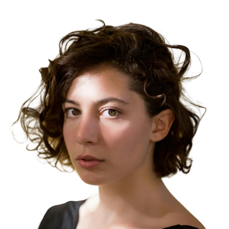 Close-up portrait of a woman with short curly brown hair looking directly at the camera against a black background.