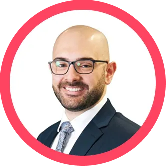 Smiling bald man with glasses in a dark suit and patterned tie inside a pink circular frame.