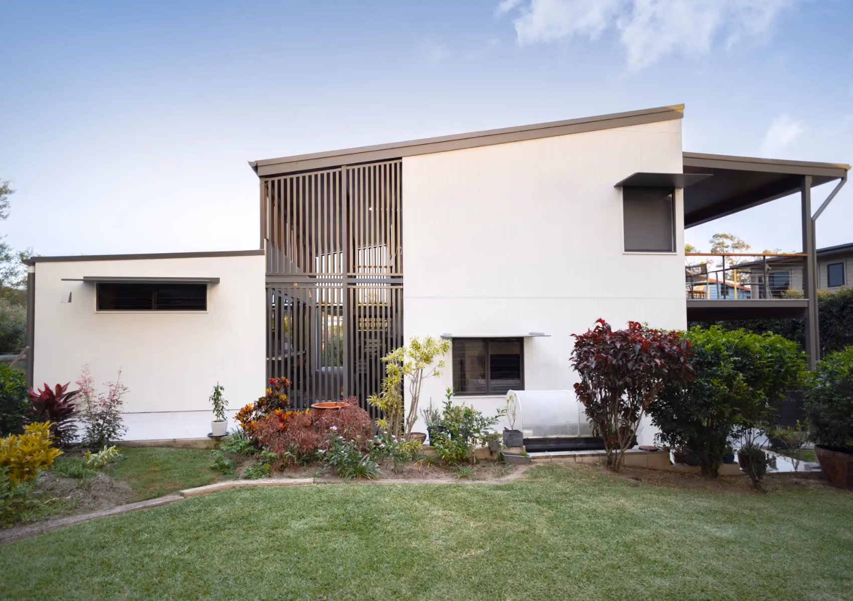 The Cubby, a white two-storey home with a vertical slat screen and tropical garden