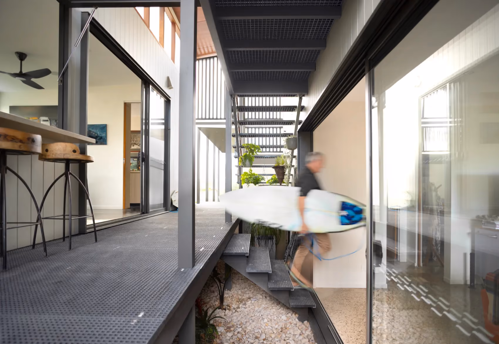 Person carrying a surfboard past the stairs on a covered walkway