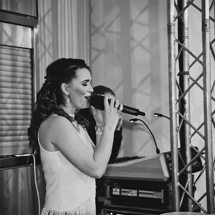 Schwarz-weiß Aufnahme: DJane Katrin Mendelsohn singt mit Mikrofon während eines Events.