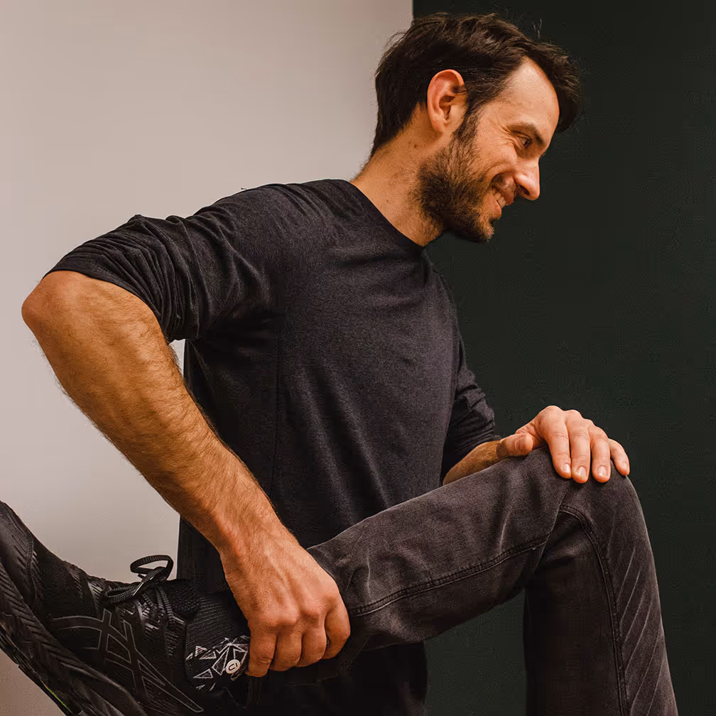 A man in fitness attire stretches his leg, preparing for a morning outdoor running activity.