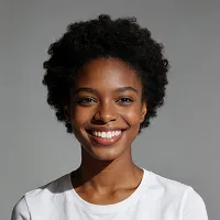 Smiling young woman with natural curly hair wearing a white shirt against a neutral gray background.