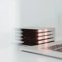 Stack of sleek black external hard drives with LED lights glowing, placed next to a laptop keyboard on a white surface.