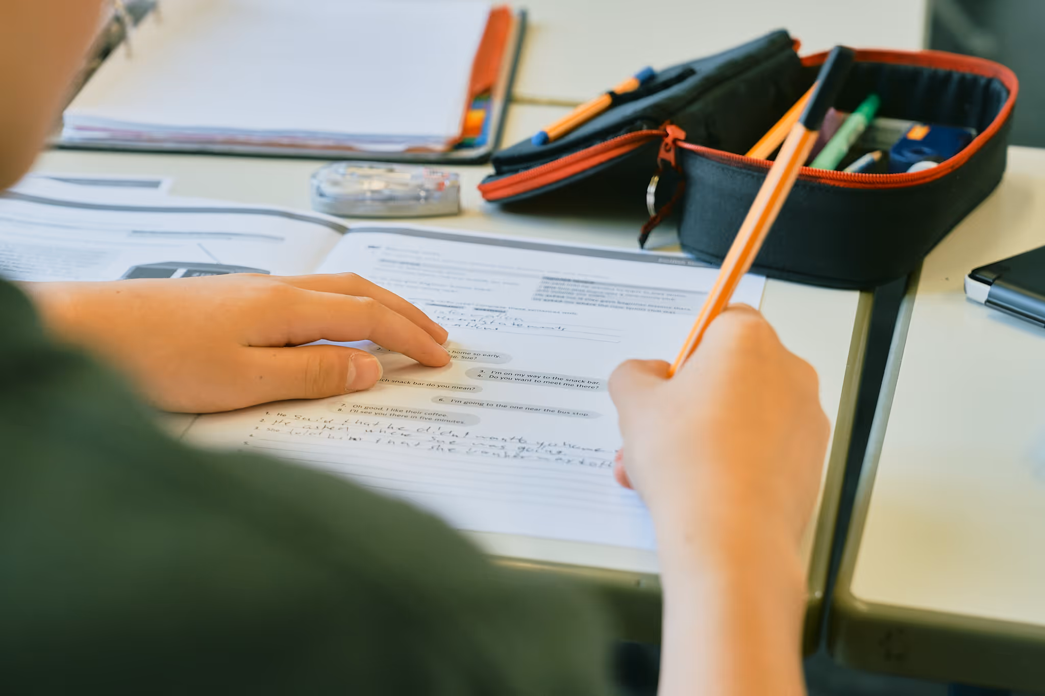 Schüler löst Arbeitsblatt mit Stiften und Federmäppchen auf dem Tisch