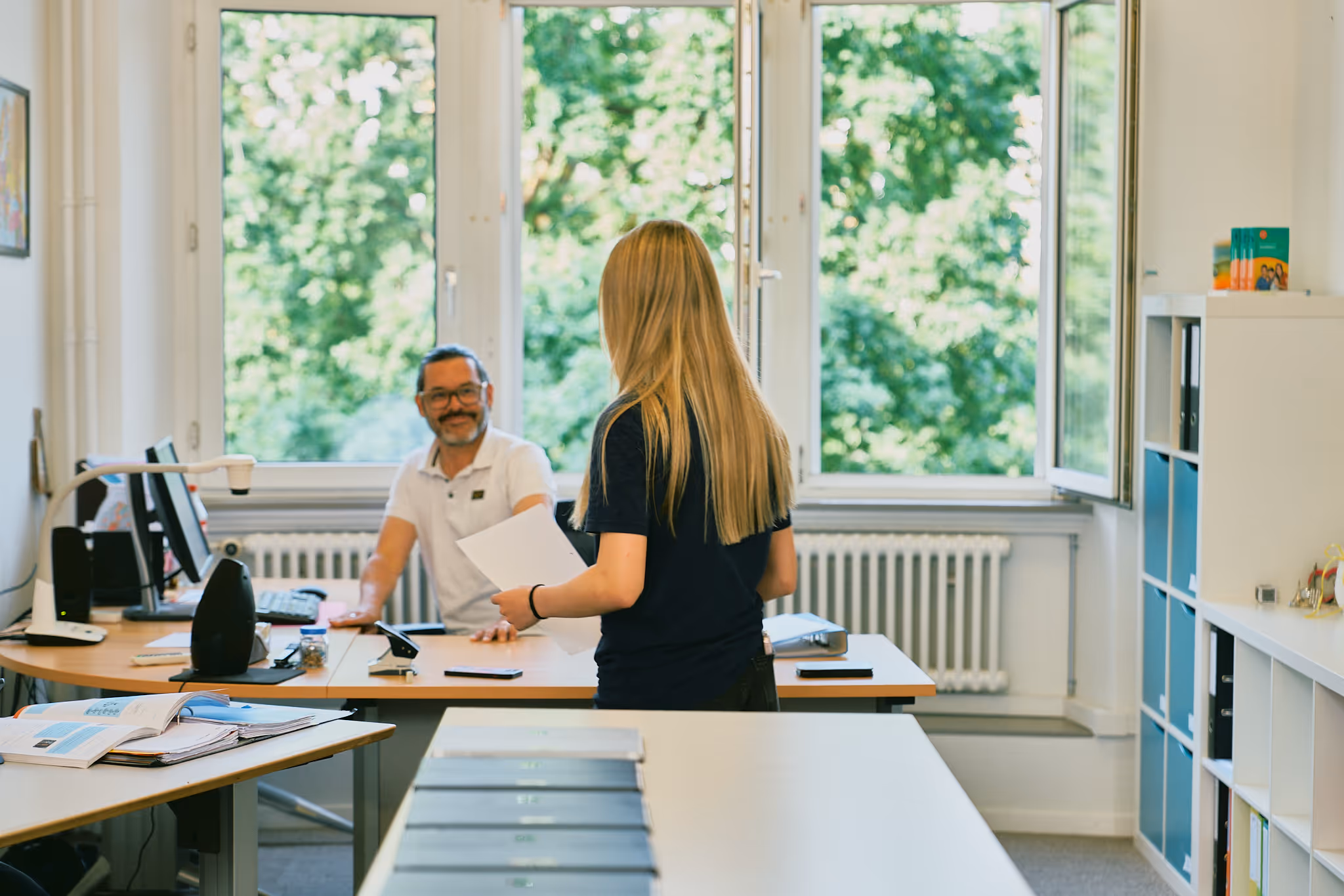 Zwei Personen in einem hellen Büro mit Blick auf grüne Bäume