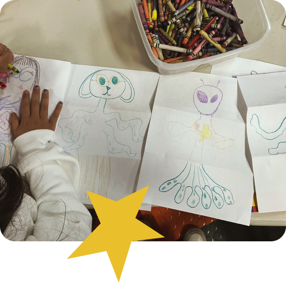 photo from above of a child drawing aliens on paper with crayons