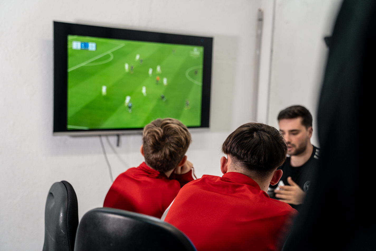 Grup de jugadors i cos tècnic analitzant un partit de futbol professional en pantalla per aprendre situacions reals de joc.