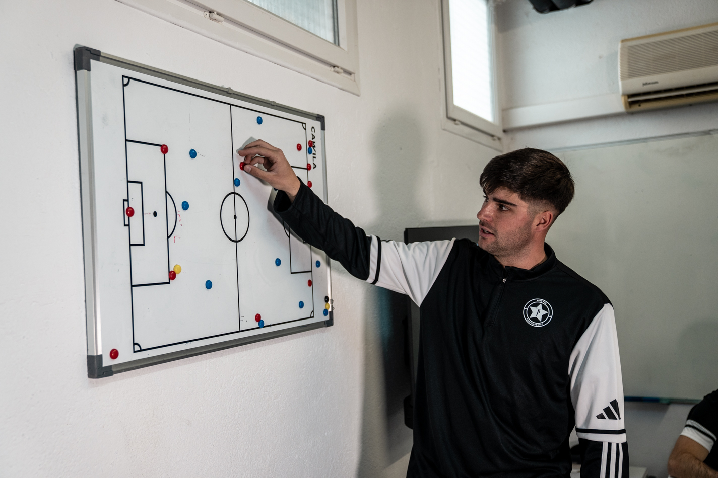 Entrenador de futbol dissenyant estratègies i jugades sobre una pissarra tàctica magnètica.