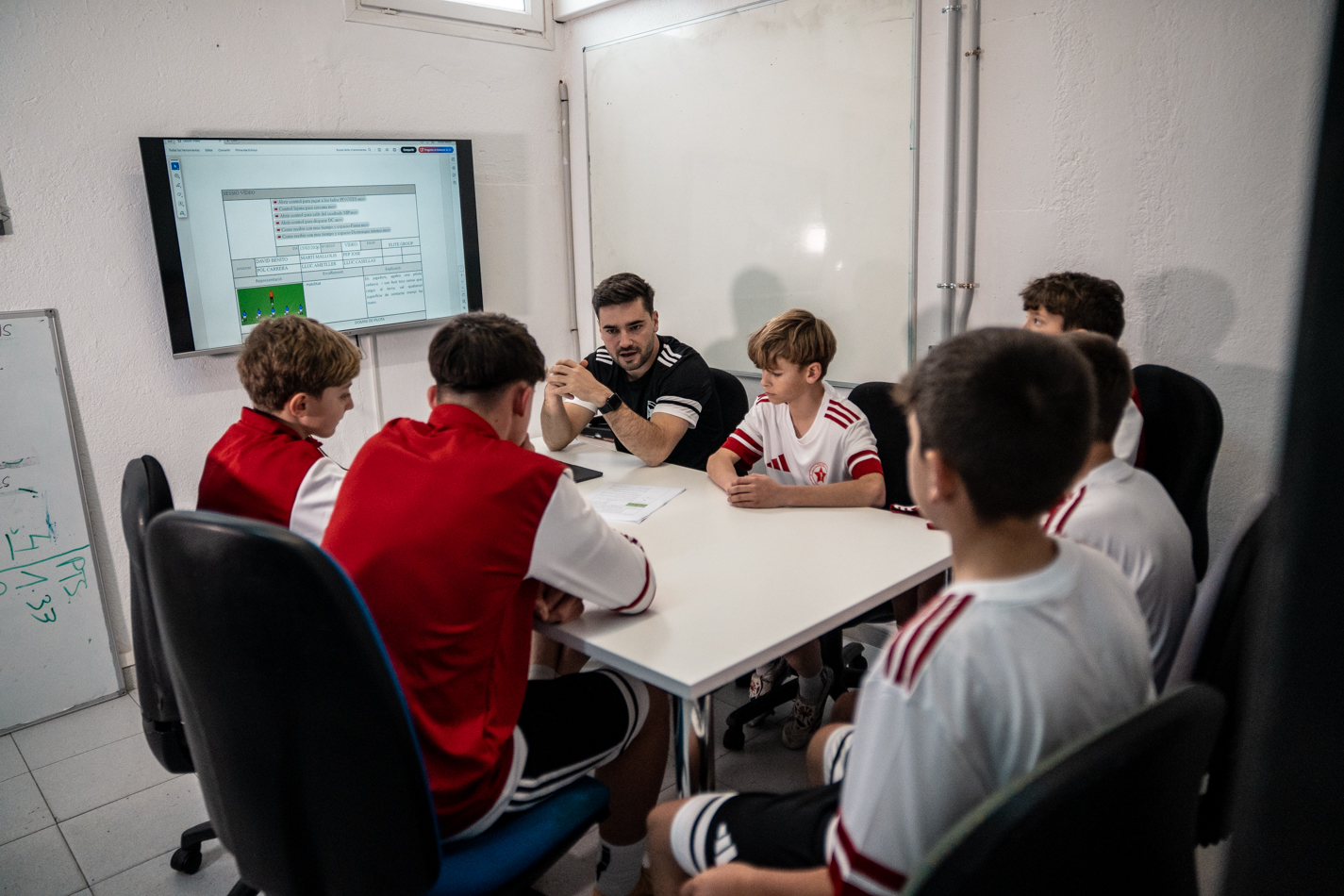 Jugadors de Prem Academy reunits a la sala de vídeo amb el seu entrenador repassant conceptes tàctics de futbol.