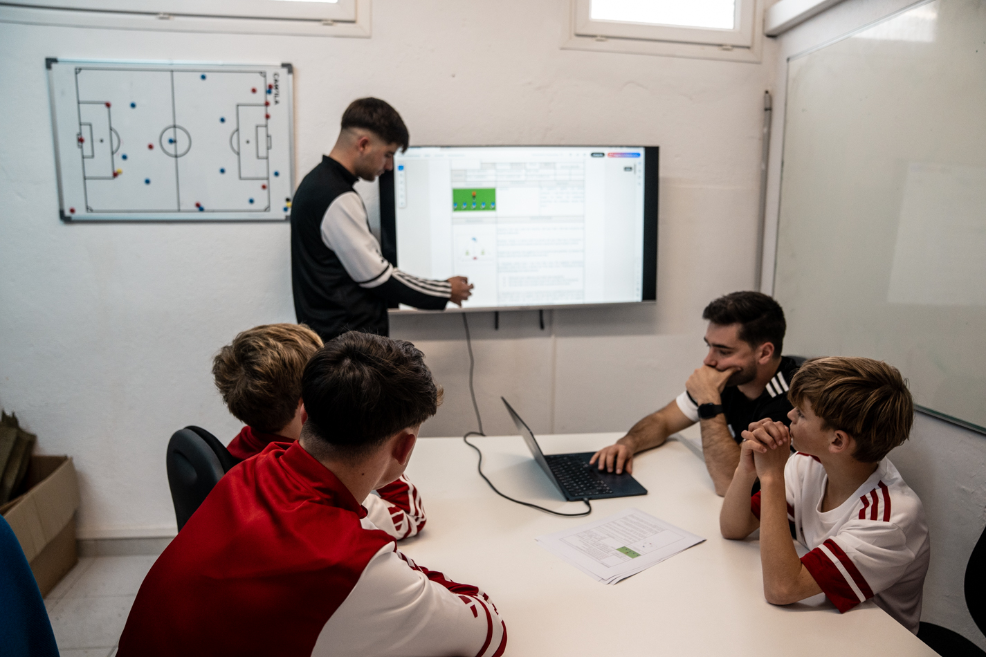 Entrenador de l'acadèmia de futbol explicant moviments i correccions en una pissarra digital tàctica.
