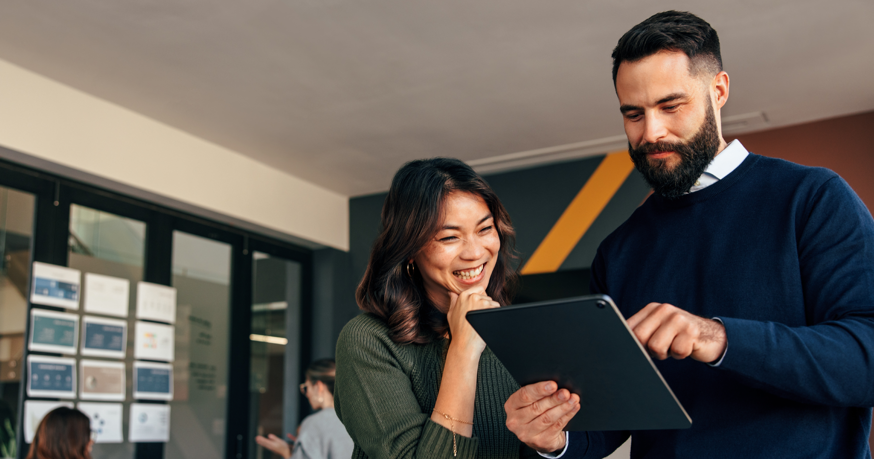 Two colleagues smiling while reviewing figures on a tablet in an office.