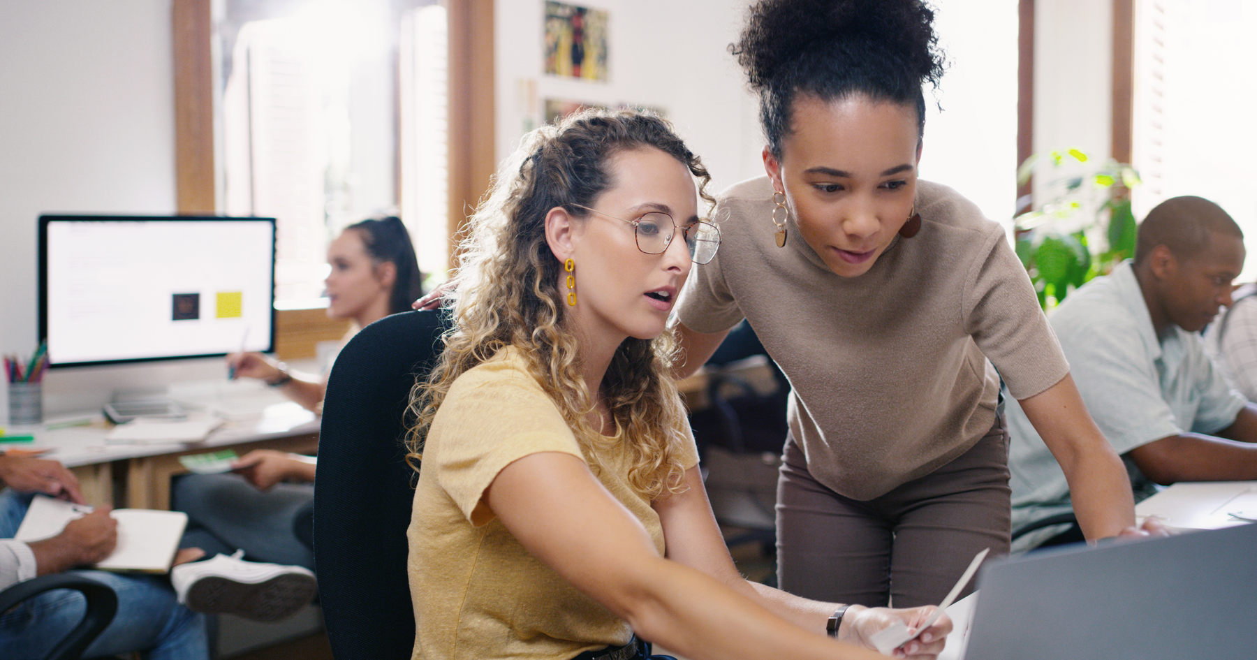 Two colleagues working together at a computer in an open office.