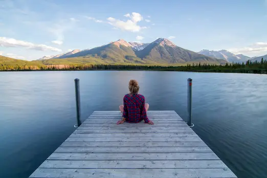 Woman standing on a dock looking out at a mountain vista, symbolising reflection, perspective and healing — Vistas Psychotherapy & Wellness