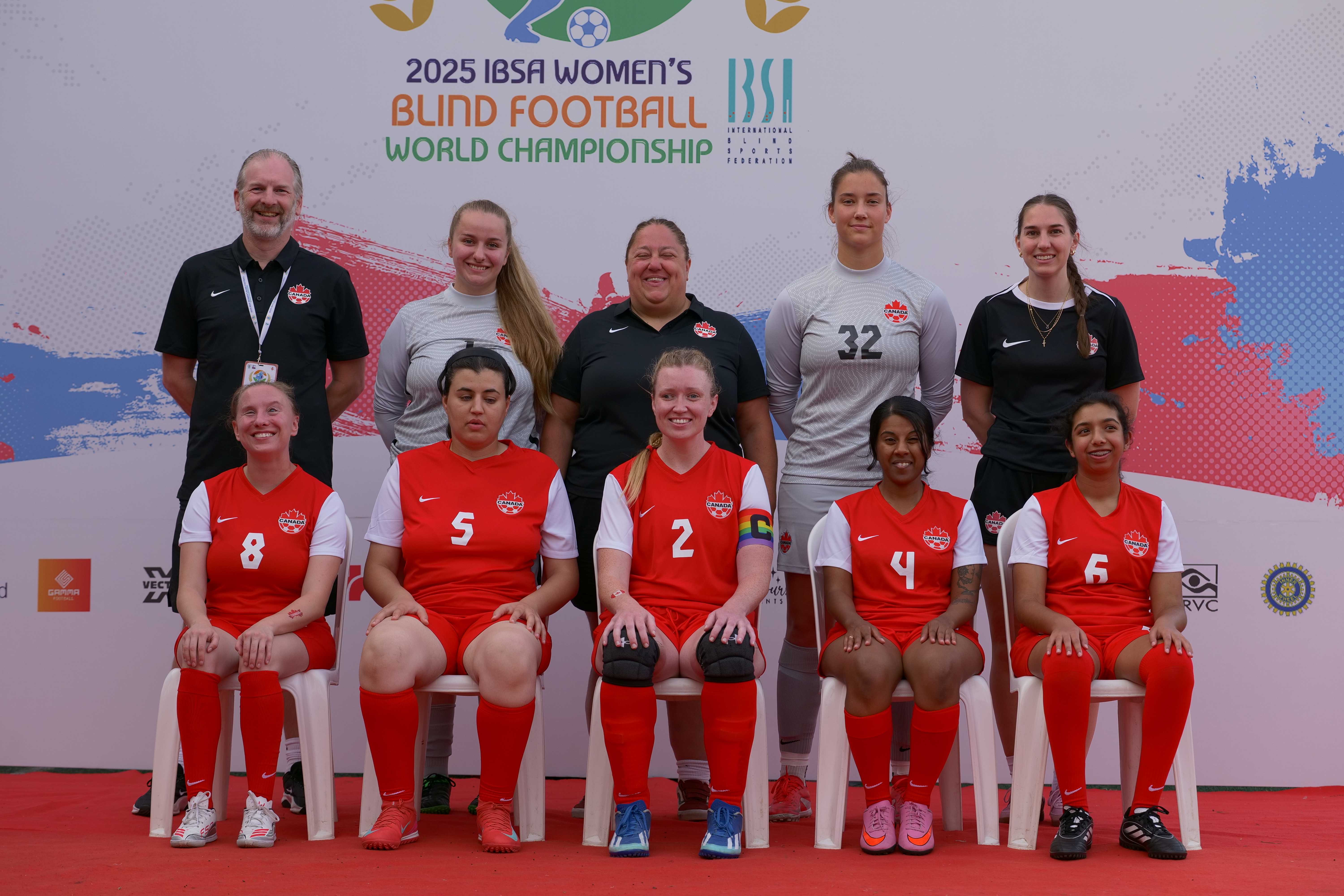 2 audible soccer balls sit on green grass with 4 players in the background.