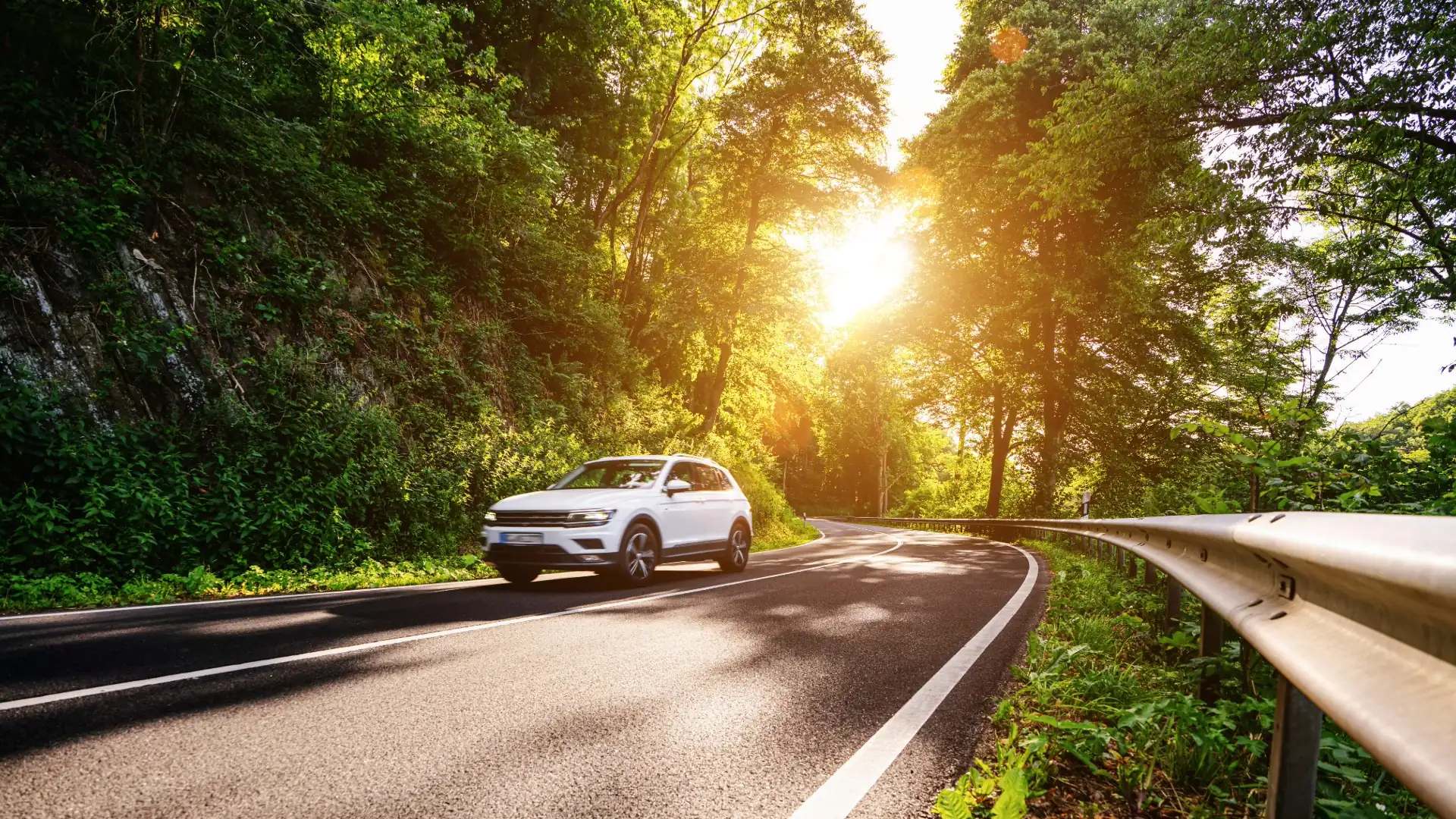 Car driving down a highway into a forest with bright sun rays through the trees