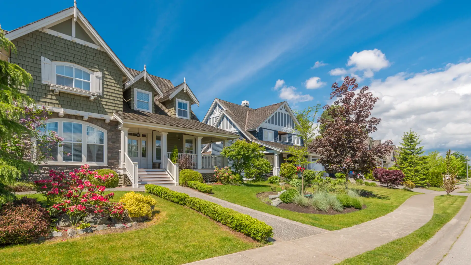 Two-story craftsman-style home with a front porch, flower beds and a curving sidewalk in a suburban neighborhood