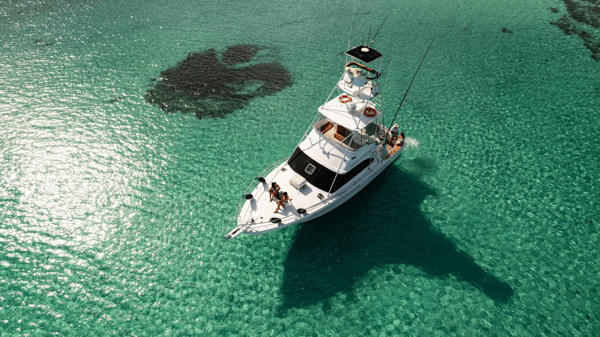 Game Time anchored in turquoise shallows with guests relaxing on the bow
