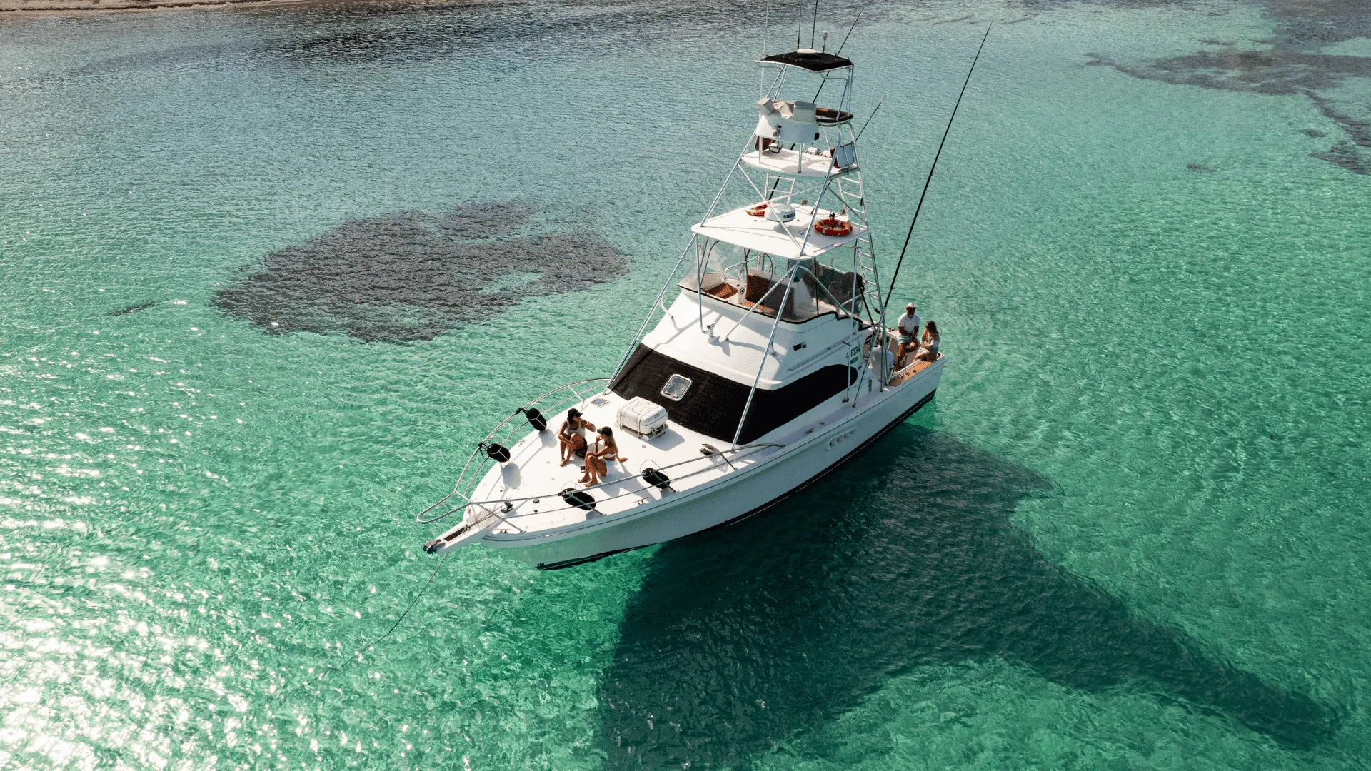 Aerial view of Game Time anchored over clear turquoise water with guests on the bow