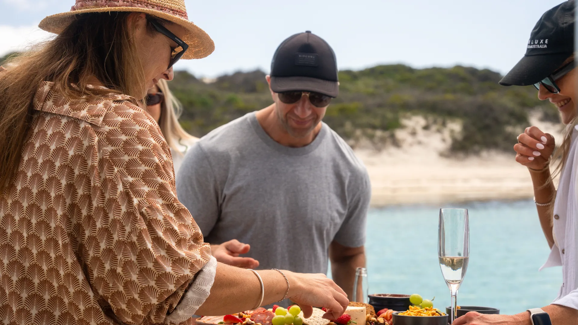 Guests helping themselves to a platter on board with a Rottnest Island beach behind
