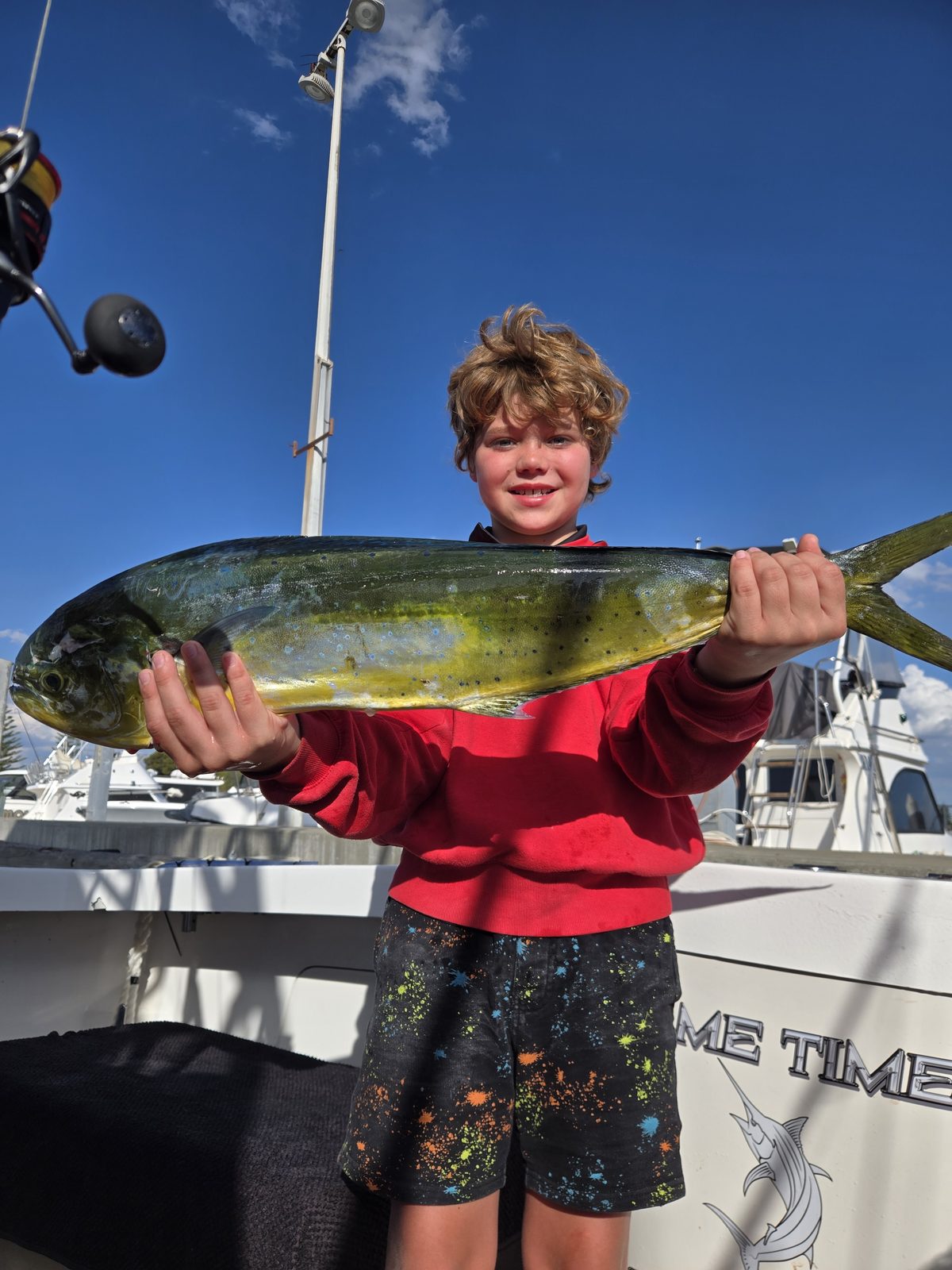 Young angler lifting a mahi mahi against a clear blue sky on a Game Time Charters charter