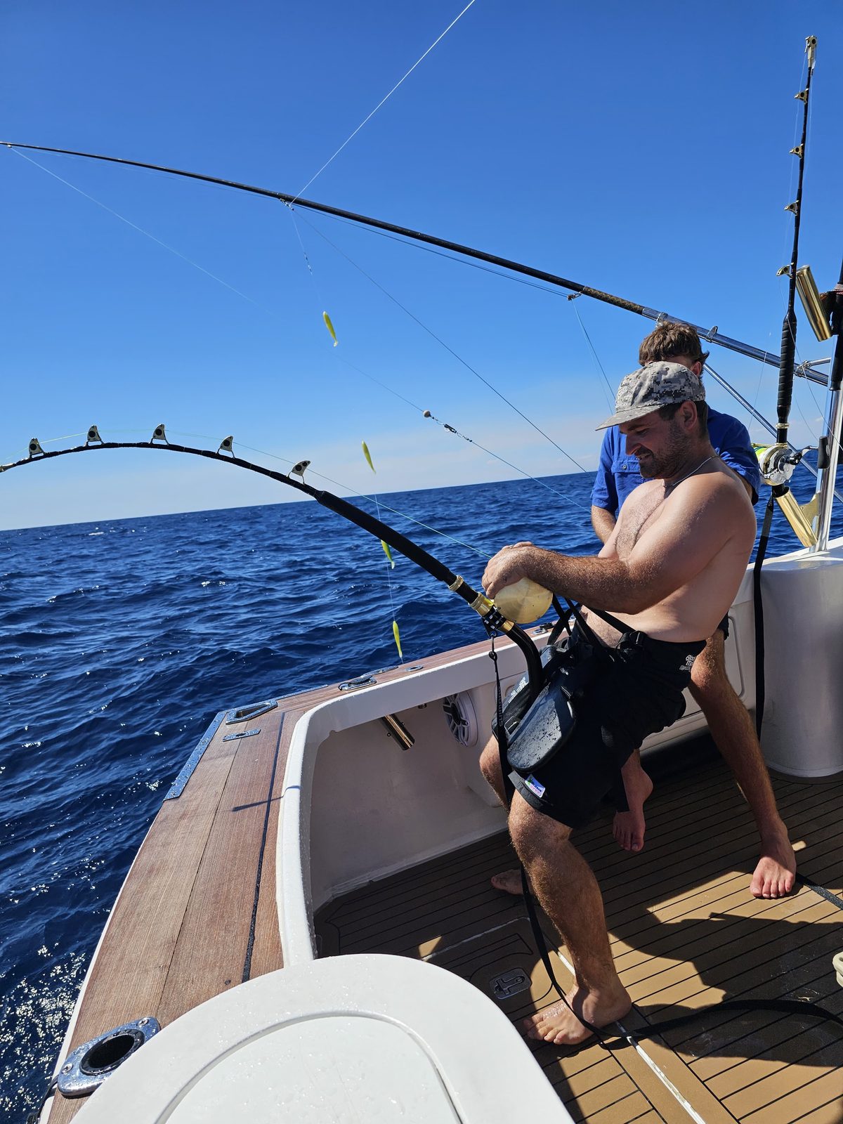 Angler harnessed into a bent rod fighting a fish on a Game Time Charters game fishing charter