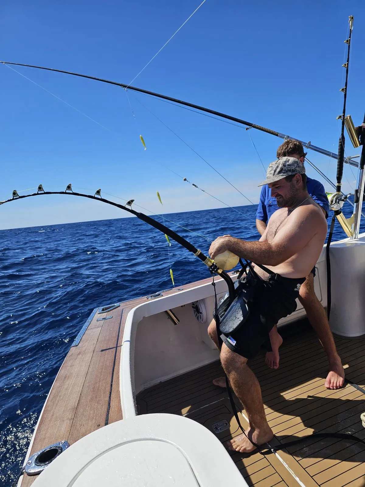 Angler harnessed into a bent rod fighting a fish on a Game Time Charters game fishing charter